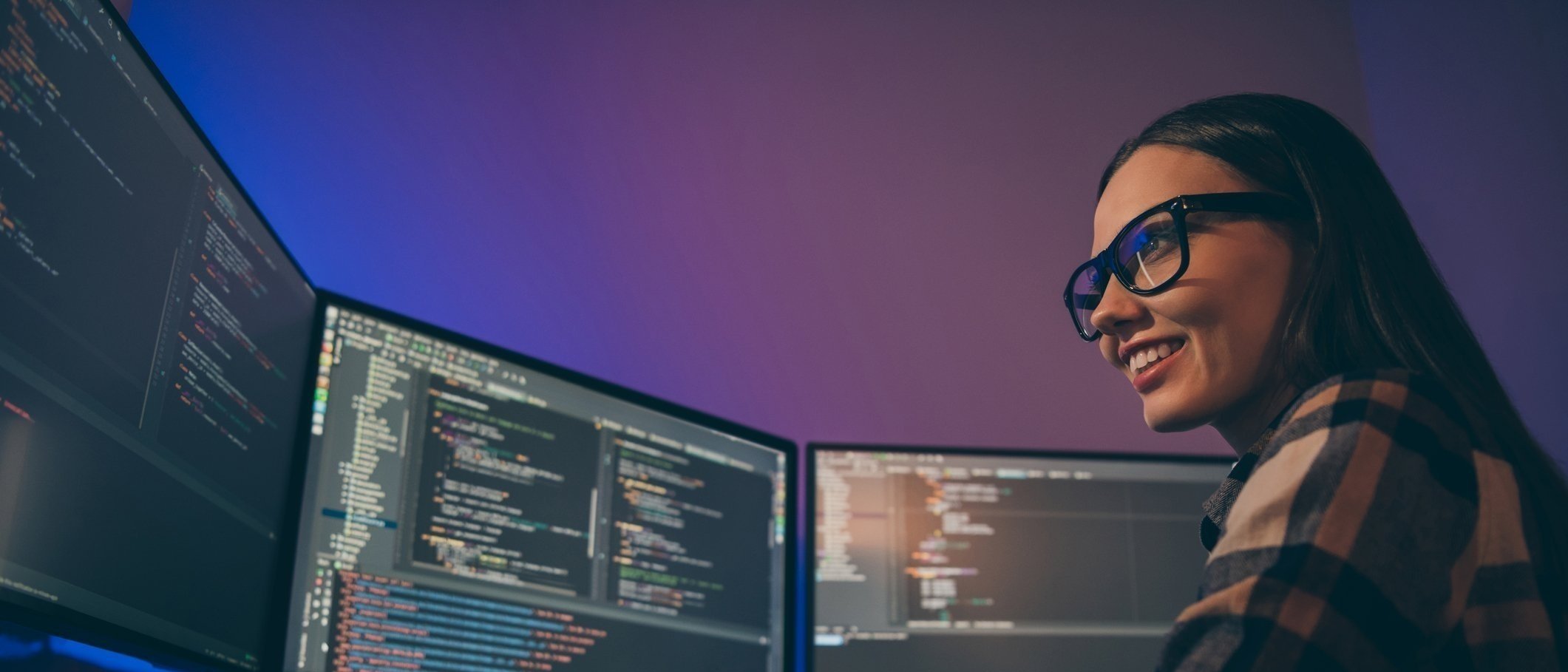 Woman looking over 3 computer screens